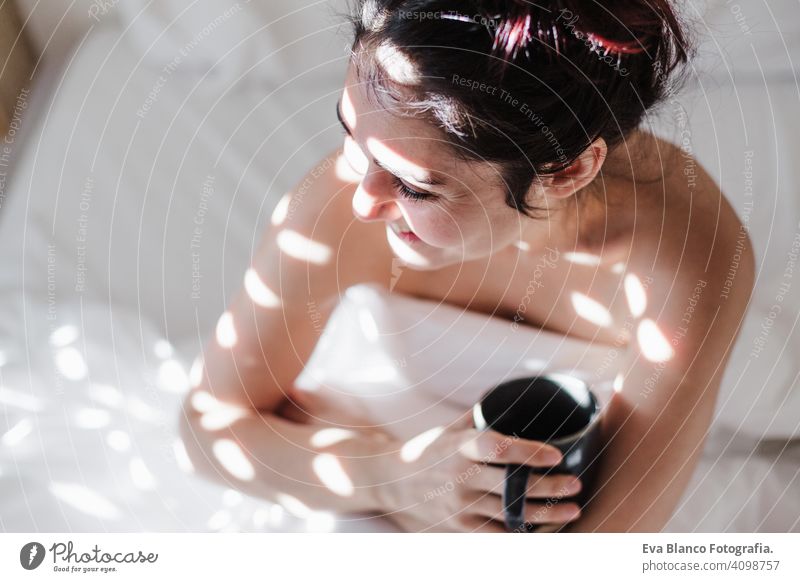 attractive young caucasian woman relaxing well in bed during morning time. Lady enjoys cup of coffee in bedroom breakfast drink beverage hot tea drinking