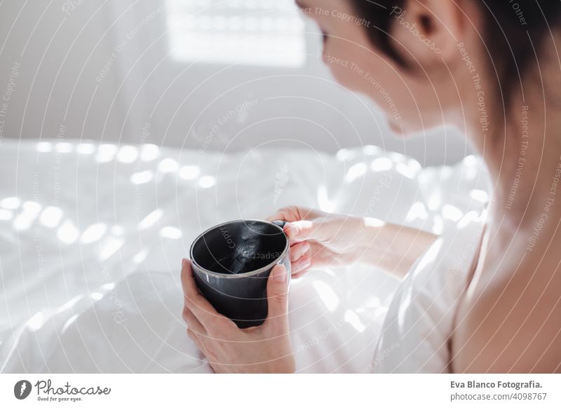 attractive young caucasian woman relaxing well in bed during morning time. Lady enjoys cup of coffee in bedroom breakfast drink beverage hot tea drinking