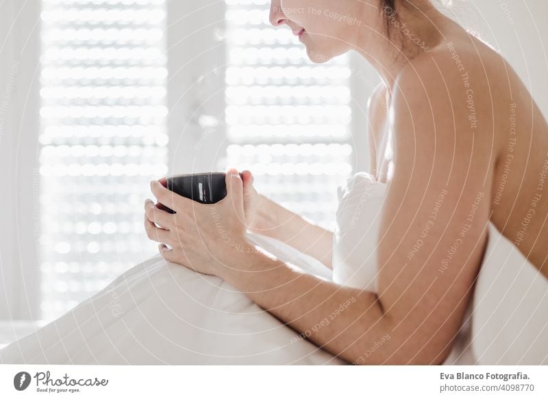 attractive young caucasian woman relaxing well in bed during morning time. Lady enjoys cup of coffee in bedroom breakfast drink beverage hot tea drinking