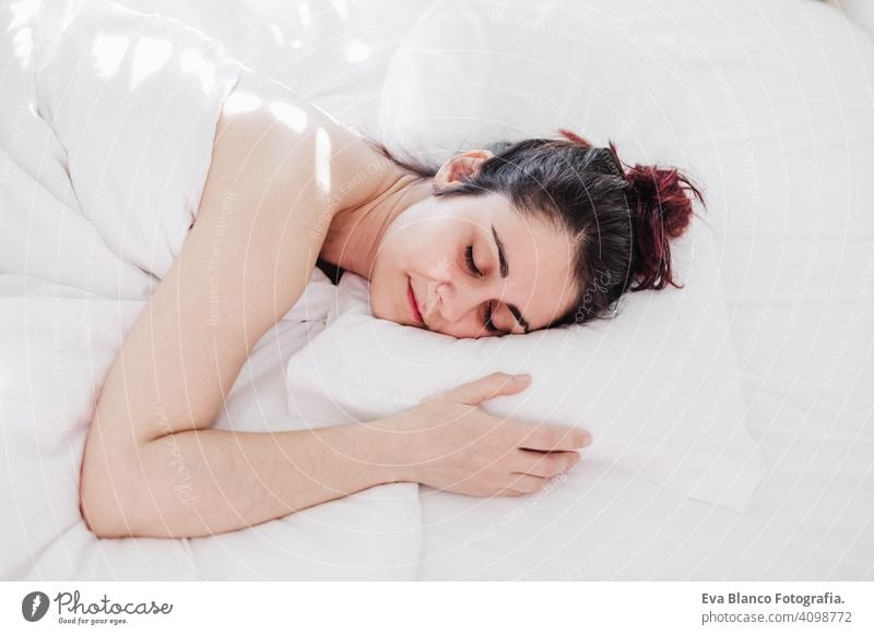 Top view of attractive young woman sleeping well in bed hugging soft white pillow. girl resting, good night sleep concept. Lady enjoys fresh soft bedding linen and mattress in bedroom