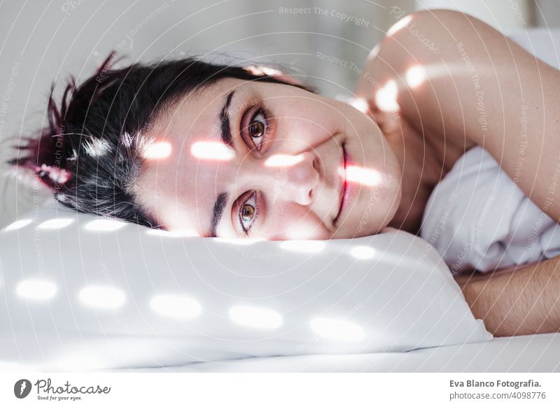 portrait of attractive young caucasian woman relaxing in bed during morning time. Lady enjoys fresh soft bedding linen and mattress in bedroom sleeping nap