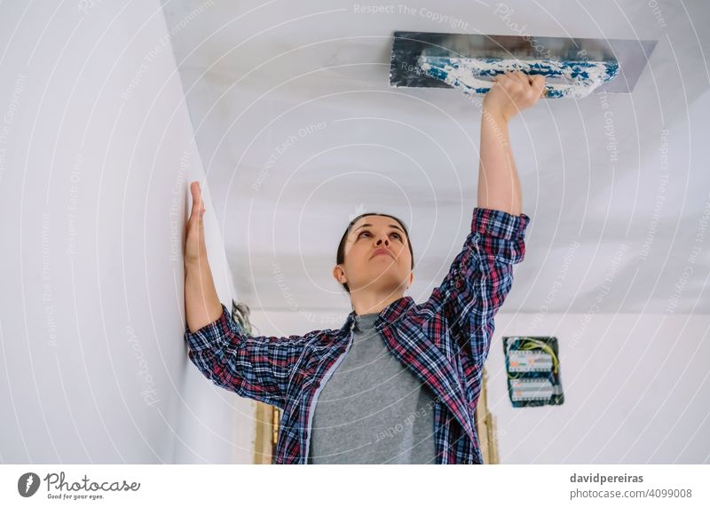 Bricklayer smoothing plaster ceiling with the trowel bricklayer woman female plasterer plastering reform installation gypsum plaster working home improvement