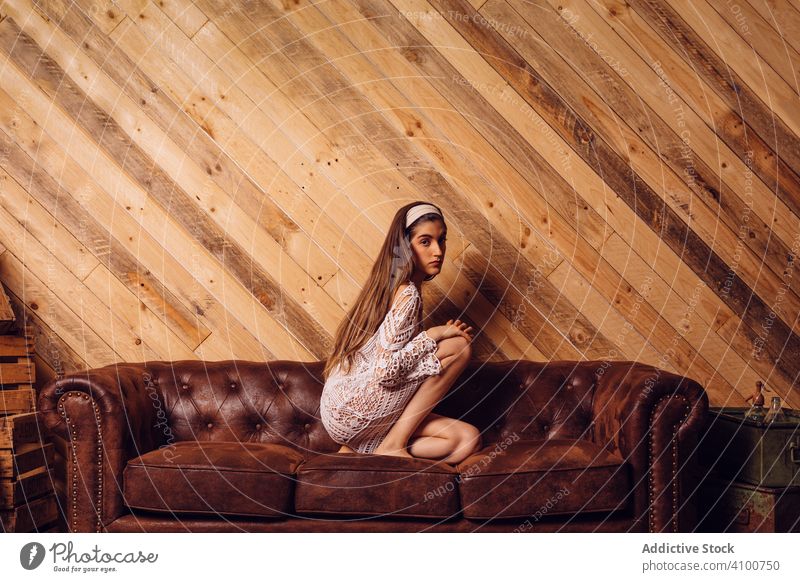 Young woman in white dress sitting on couch young interior female hipster brown legs fashion portrait person wooden room people girl sofa caucasian model hair