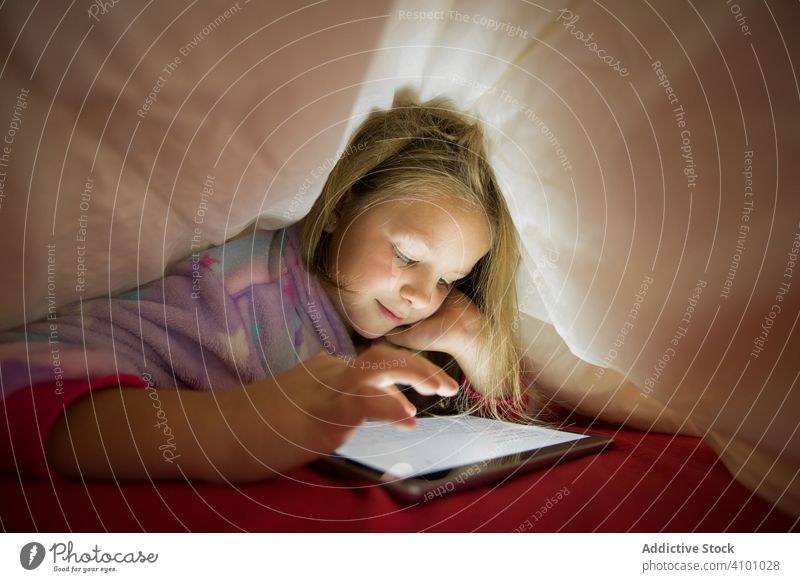 Girl using tablet under blanket girl bed hide watching playing bedtime pajama lying child happy fun positive enjoy red white kid preschooler cute little