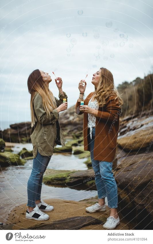 Happy female friends blowing bubbles on seashore women sister coast stone together rock fun bonding love happy playful close carefree seaside cheerful enjoy