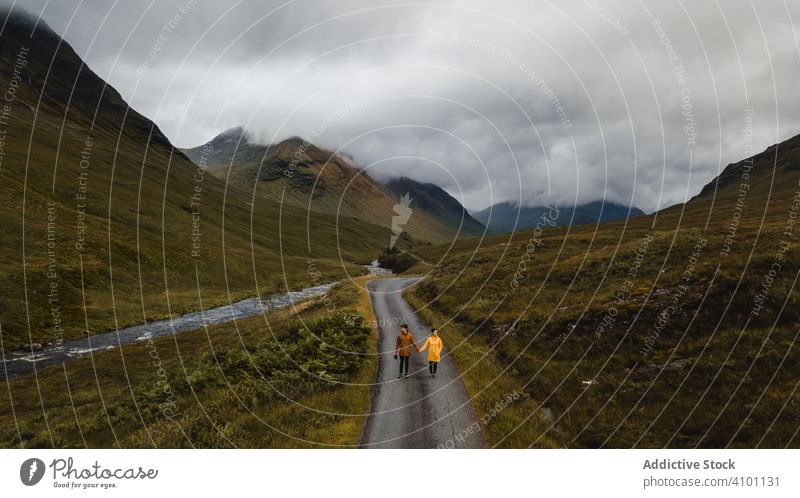 Tourists standing on road near stream in meadow against mountains in thick clouds couple tourism hiking highland valley scotland adventure trip peace travel sky