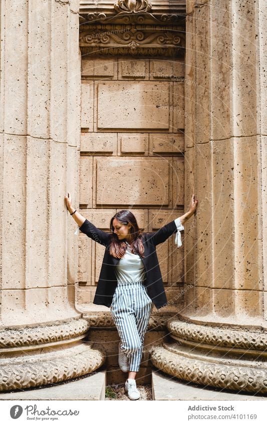 woman leaning on pavement between tall massive columns and looking down in San Francisco ancient geometric architecture park support female adult design