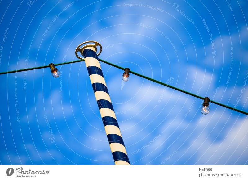 Chain of lights on blue and white decorated pole of beer garden in front of blue sky Beer garden beer garden season blue white Spring Summer out Gastronomy