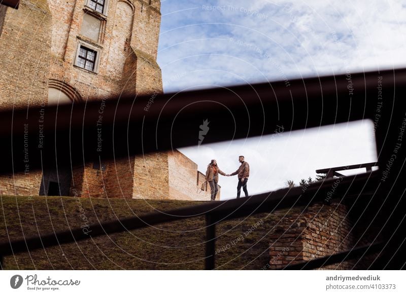 Attractive young couple walking near castle. Wife and husband are walking holding hands on background of ancient building. Two smiling lovers. selective focus