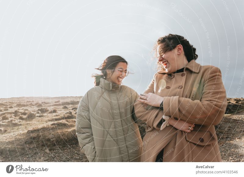 A couple of multicultural women holding each and smiling other while smiling during a sunny day with the sun reflecting in the mountains with copy space person