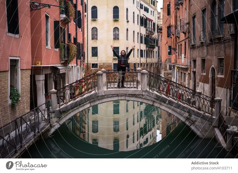 Satisfied resting woman delighting in vacation on small bridge above waterway tourism city canal building old historical standing raising hands fun architecture