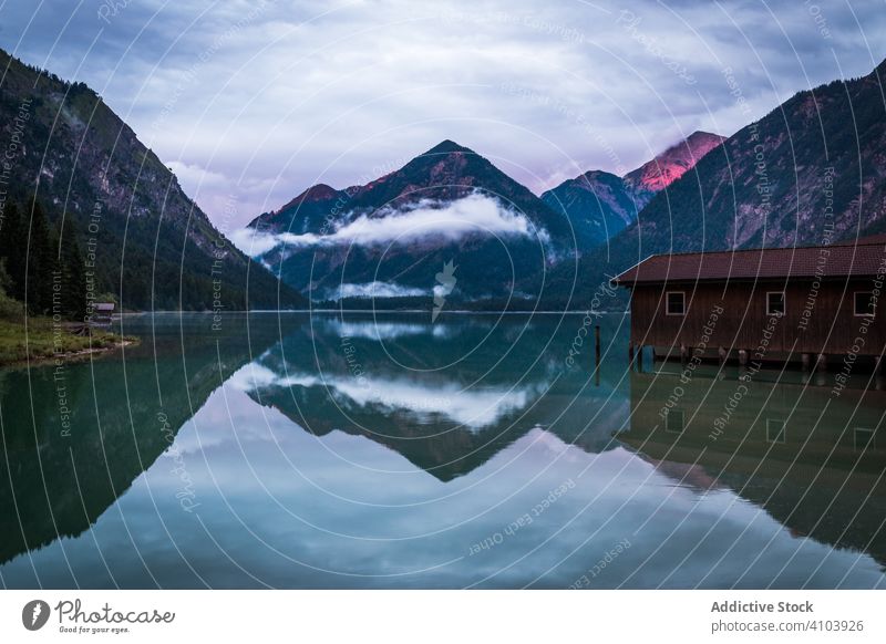 Boat shed near calm lake in mountains water cloudy countryside alpine ridge austria old aged shabby weathered shelter structure construction building storage