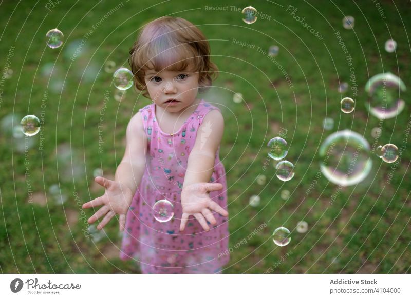 Joyful girl playing with colorful bubbles in grass soap childhood joyful fun adorable cheerful park playful enjoyment action wet little motion recreational blow