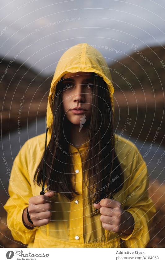 Traveler in yellow raincoat standing on shore of lake tourist nature water relax travel solitude calm tourism female forest adventure river scenery hood