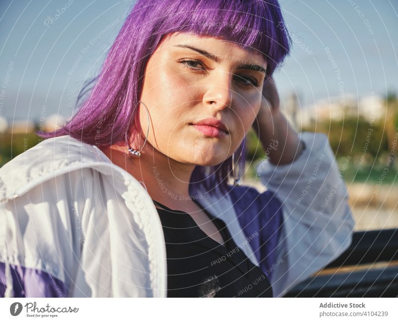 Woman with purple hair leaning on metal fence woman touching stylish urban hairstyle jacket shiny district confident fashion young model street human female