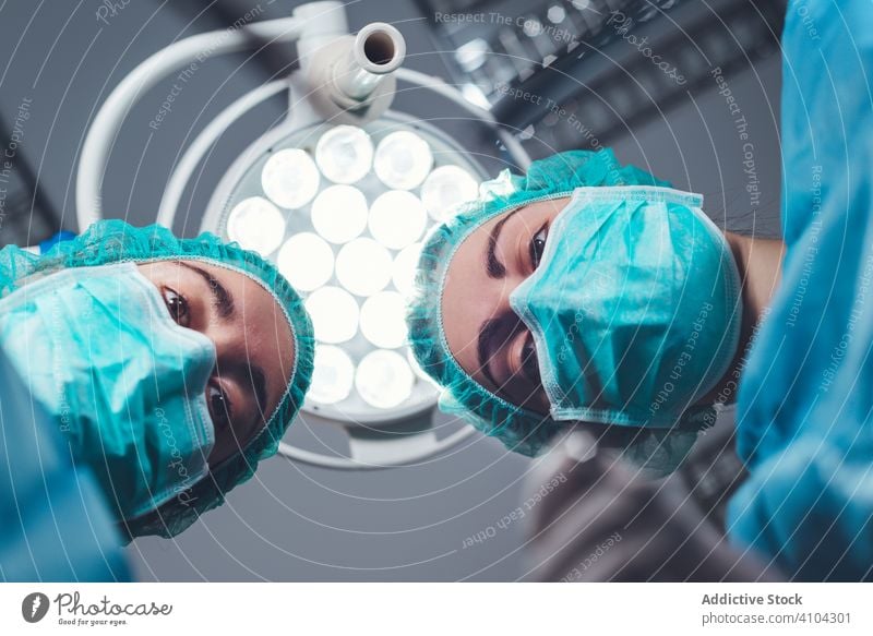 Women performing surgery in hospital together surgeon operating theater lamp tool mask hat women work doctor healthcare female sterile instrument colleague job