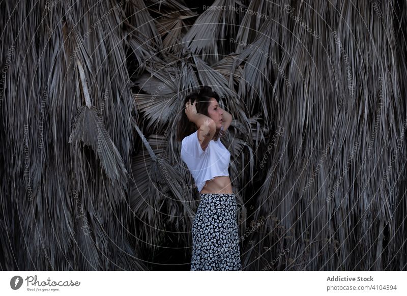 Carefree woman touching hair among grey dry leaves tropical plants leaf light fix foliage summer standing carefree freedom female nature exotic wild lifestyle