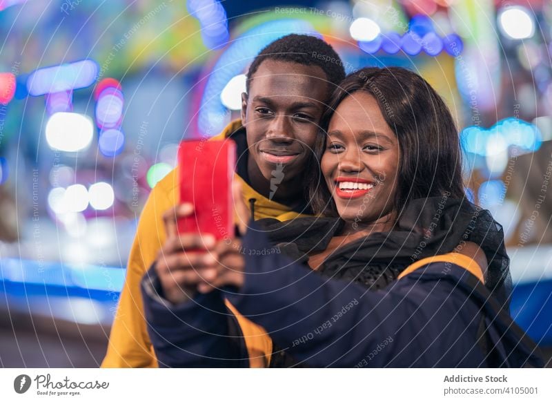 Black couple taking selfie on fairground smile smartphone ethnic night colorful illumination entertainment man woman fun boyfriend girlfriend black funfair