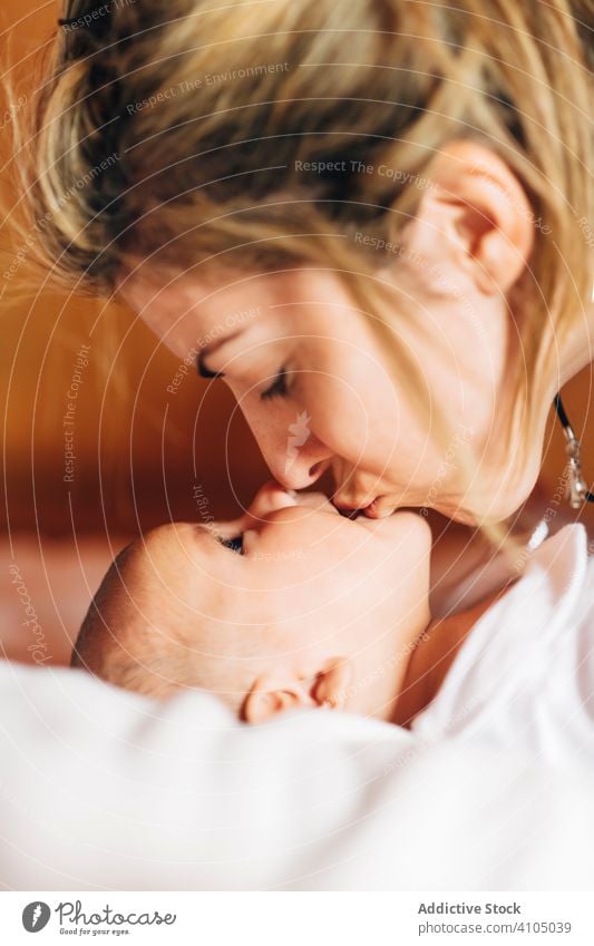 Bright mother touching nose by nose of baby play happy bonding care newborn affection lying bed home infant open mouth adorable leisure child small cute kid