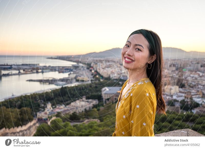 Happy ethnic tourist against city and sunset sky woman tourism smile sea castillo gibralfaro malaga spain female ruin travel trip journey coastal cityscape