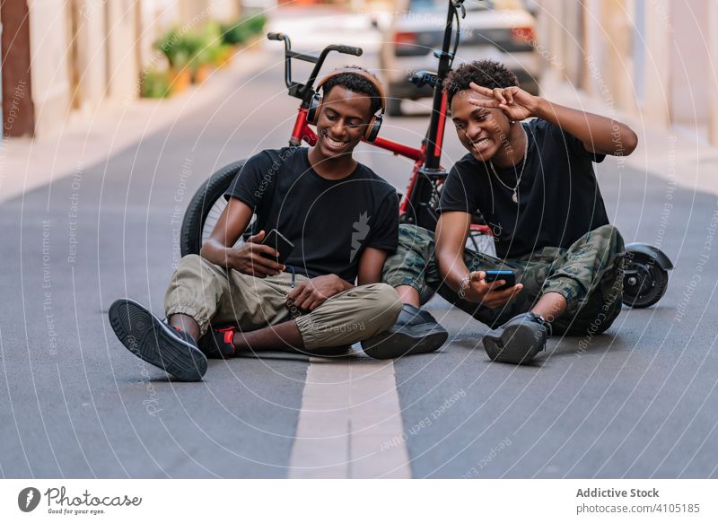 Happy young black male hipsters using smartphones in street friend generation teenager share cool picture cellphone headphone together road asphalt lifestyle