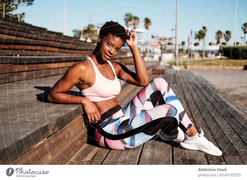 Pensive millennial ethnic athlete relaxing after training on wooden stairs in park sportswoman confident motivation serious physique slim aspiration athletic