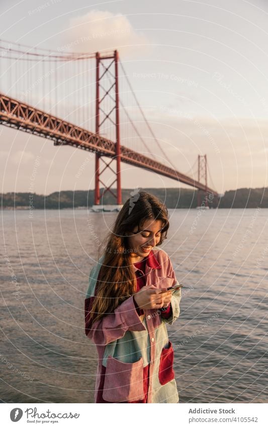 Happy woman surfing smartphone against bridge using mobile phone messaging happy leisure relax female lisbon portugal communication connection internet