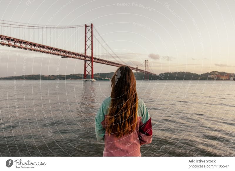 Woman standing by river against bridge woman travel tourist vacation explore waterfront view female lisbon portugal architecture freedom casual lady attraction