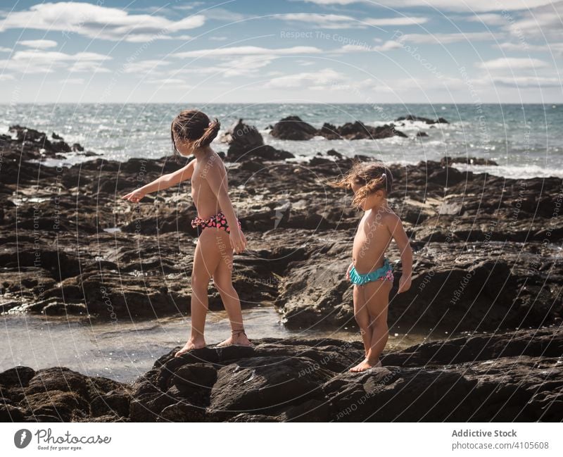 Sisters on stones near sea sister shore pointing resort sunny daytime girl summer together sibling kid child family panties barefoot show demonstrate gesture