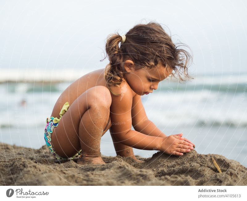 Little girl building sand castle on beach play sea heap sit haunches kid summer vacation season child ocean water lifestyle rest relax shore coast joy calm