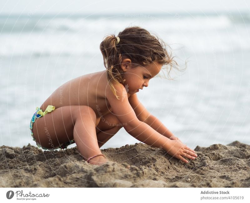 Little girl building sand castle on beach play sea heap sit haunches kid summer vacation season child ocean water lifestyle rest relax shore coast joy calm