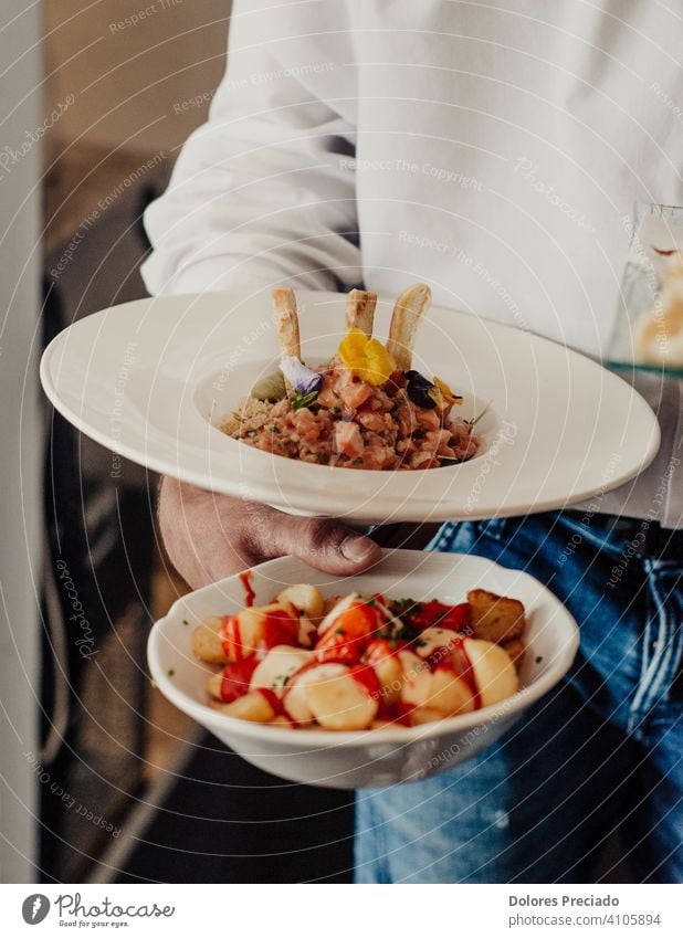 Restaurant waiter carrying a serving of spicy Spanish potatoes and a serving of salmon tartare local food cuisine local cuisine gastronomy snack eating