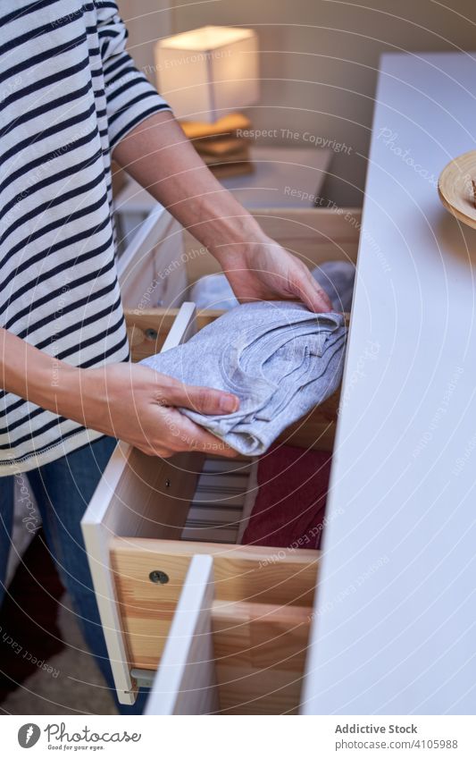 Crop woman arranging clothes in drawer cabinet arrange put home clean laundry routine household female domestic apartment flat dresser t shirt apparel