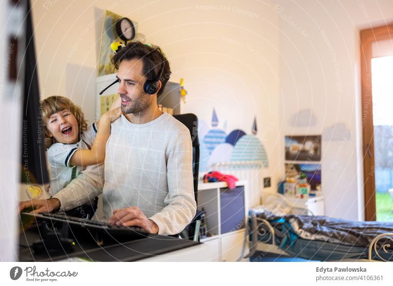 Young man working from home with his little son as a company single father working at home computer busy laptop life balance coronavirus covid social distancing