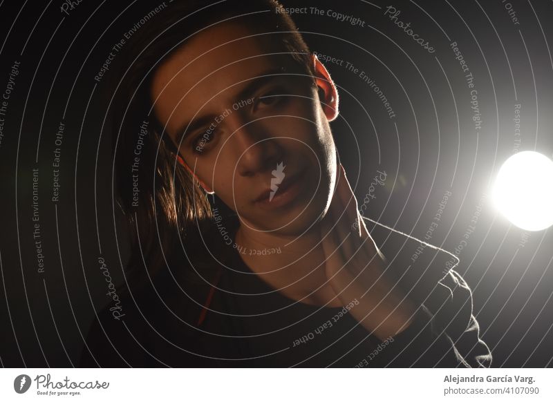 Long haired young handsome man on a black background with a light illuminating his face, with a flirtatious expression for the camera showing a slight smile art