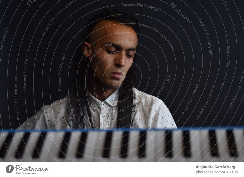 Conceptual music photography, keys of piano in the foreground with a long haired man musician in the background with a peaceful expression, black background