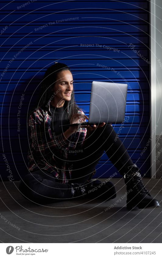 Beautiful brunette woman with plaid shirt and black pants sitting in front of the door of a storage room. He has a portal computer with which he works and organizes the moving boxes