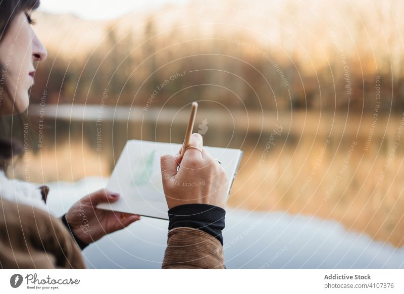 Woman standing at lakeside and drawing in notebook woman forest landscape tranquil nature autumn picture painter scenic female young artist water tree beauty