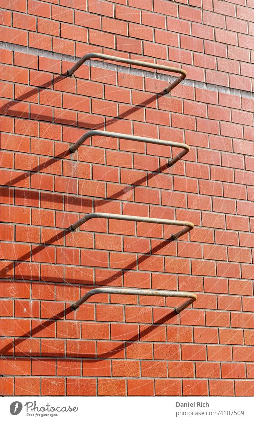 4 iron bars that are part of an escape ladder in case of a fire, are caught in the setting sun. The shadows make it look like 3 bent rectangles and 1 perfect one.