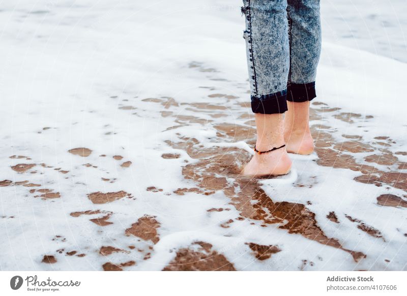 Woman in jeans standing on beach with sea foam woman barefoot wave water ocean travel sand female nature coast relax adventure alone vacation holiday recreation