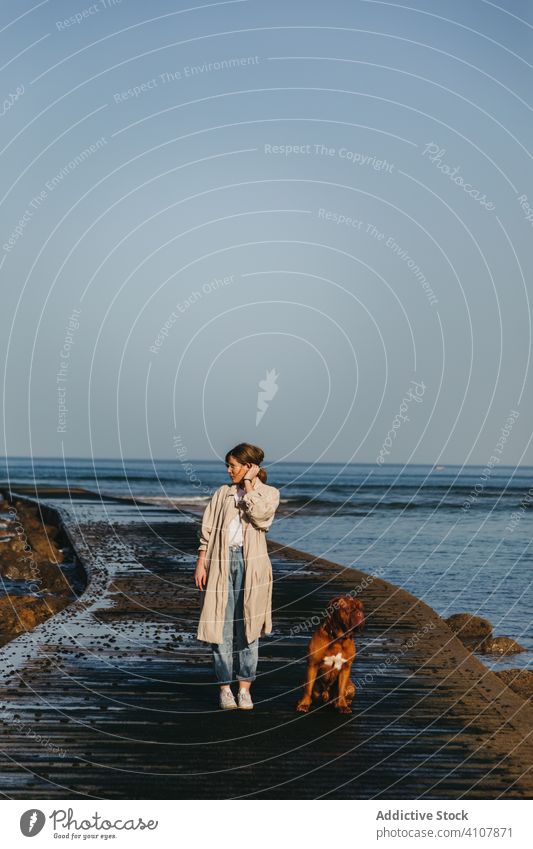 Woman with dog walking along wet pier against calm sea water and rocky coast in sunny day woman companion fresh pet ocean spain tranquil mastiff owner beach