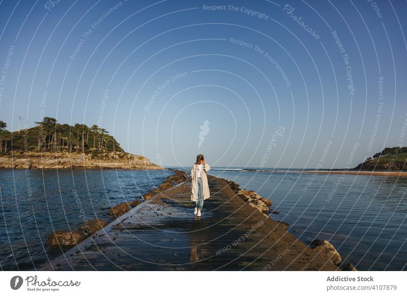 Woman walking alone along pier against troubled ocean water in windy weather woman waterfront wave sea coast shore travel adventure beach spain female casual