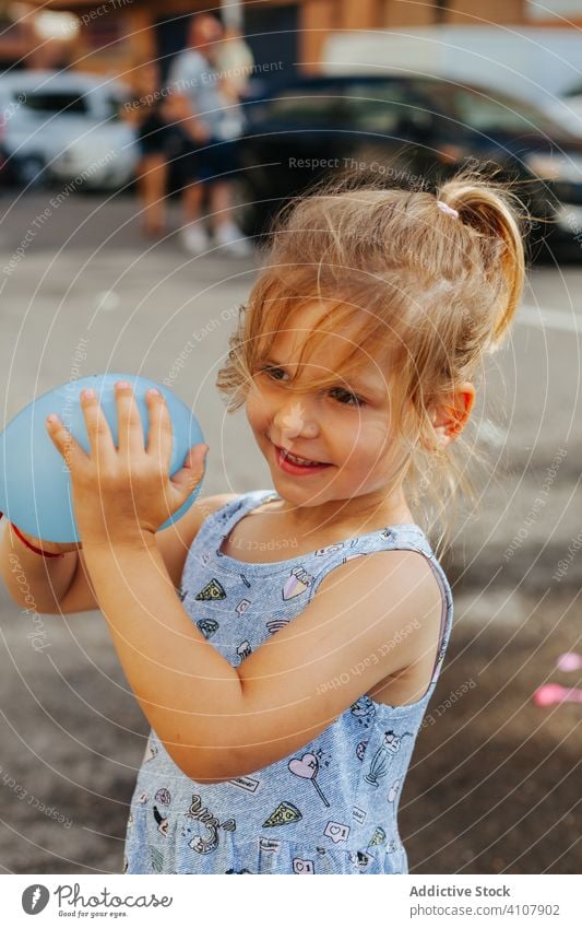 Girl with water balloon on street girl sidewalk summer water bomb play town sunny daytime kid child city pavement toy cute adorable childhood innocence weekend