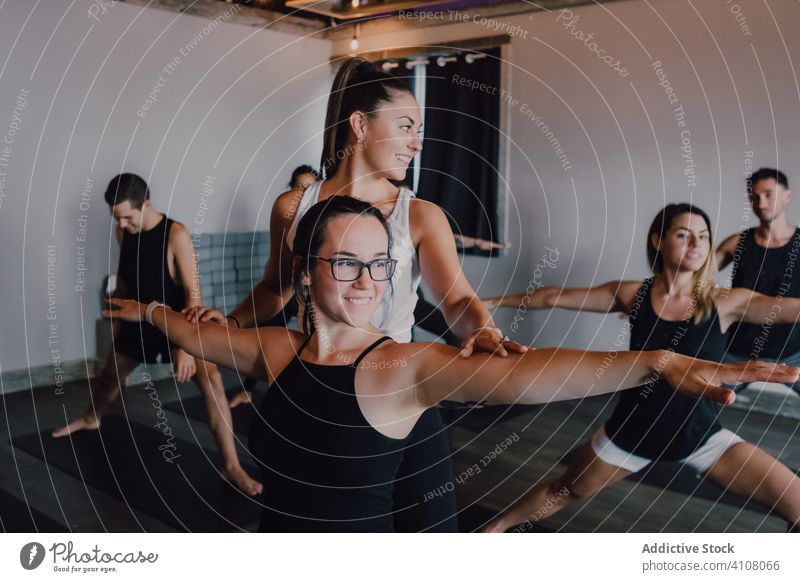 Young sporty people stretching body practicing yoga in warrior pose with trainer in light contemporary studio help exercise practice balance mat class smile