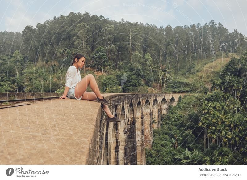 Asian woman sitting on railroad on bridge in tropical landscape travel exotic conetnt tourism relax female casual green forest ethnic tree plant asian sky