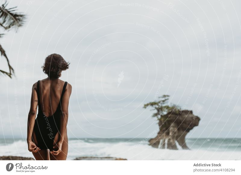 Unrecognizable female traveler in swimwear on lonely ocean beach woman storm tropical wind seashore carefree freedom tide overcast sky nature swimsuit sand