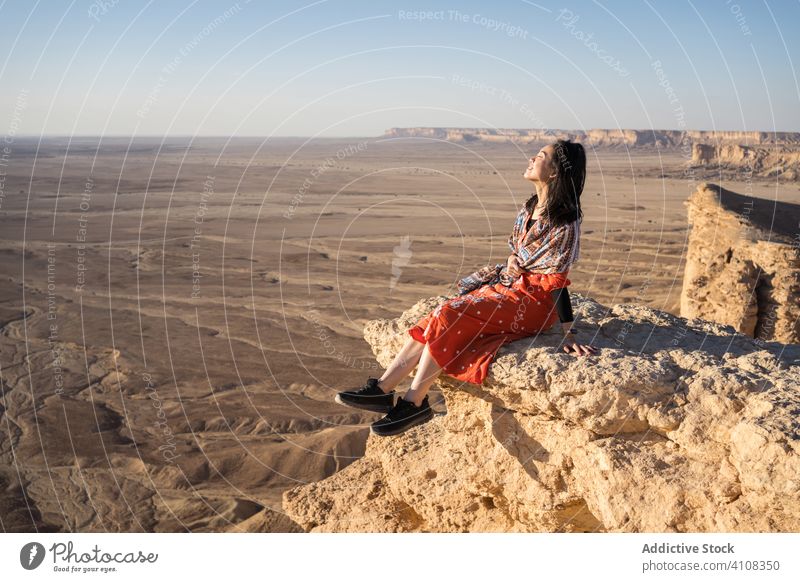 Ethnic female tourist contemplating horizon in desert contemplate woman cliff rest nature travel adventure rock freedom journey vacation terrain tourism explore