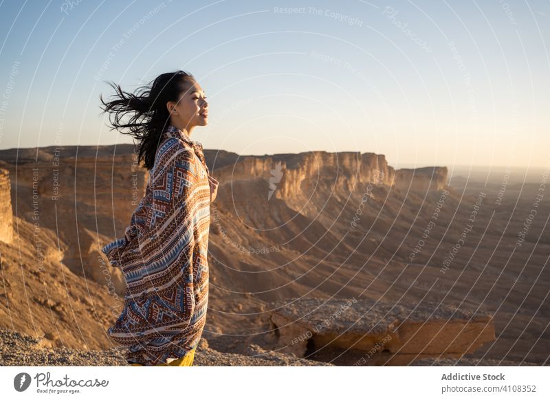 Ethnic female tourist contemplating horizon in desert contemplate woman cliff rest nature travel adventure rock freedom journey vacation terrain tourism explore