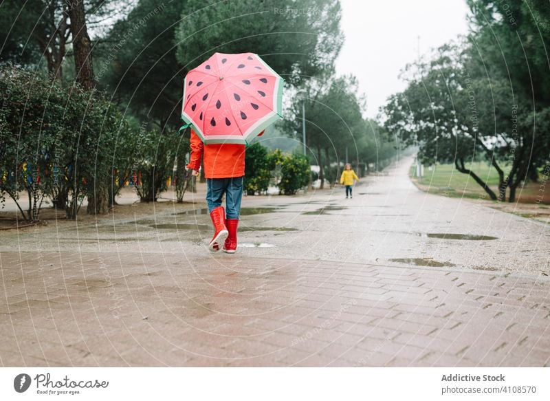 Cute child with colorful umbrella walking in park alley rain season funny water wet dirt childhood mud autumn game active weather rubber boots raincoat