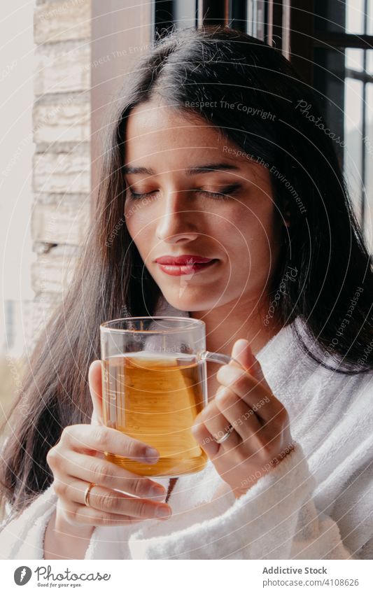 Relaxed woman in bathrobe enjoying tea relax rest drink morning window mug cozy casual female beverage cup glass lifestyle lady young home comfort pleasure warm